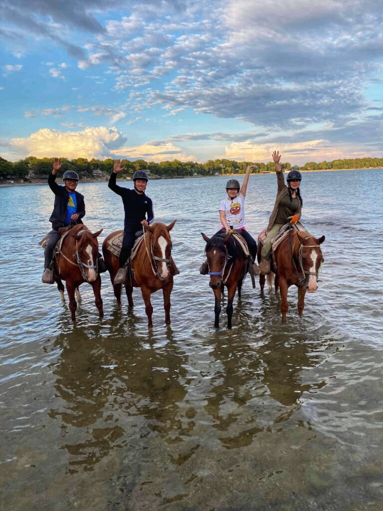 Group of horseback riders waving in water at the beach