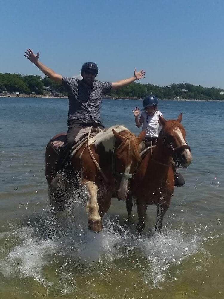 Father and daughter on horseback in the water.