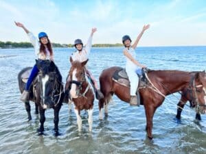 Girls on horseback in the water at the beach