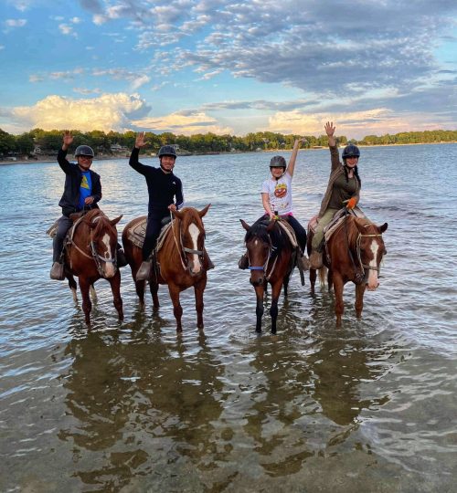 Group of horseback riders waving in water at the beach